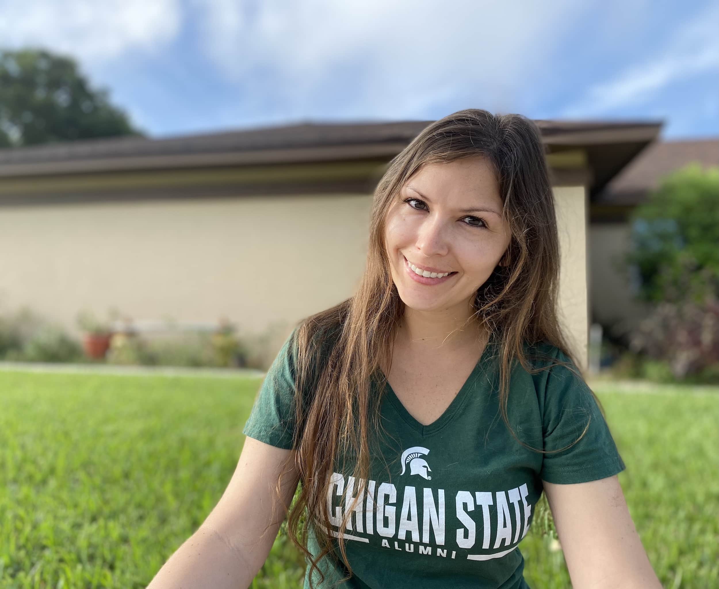 Photo of Lori Klymko-Pickup-Crawford, the author of this page, sitting in the grass in front of a house wearing a green MSU shirt.