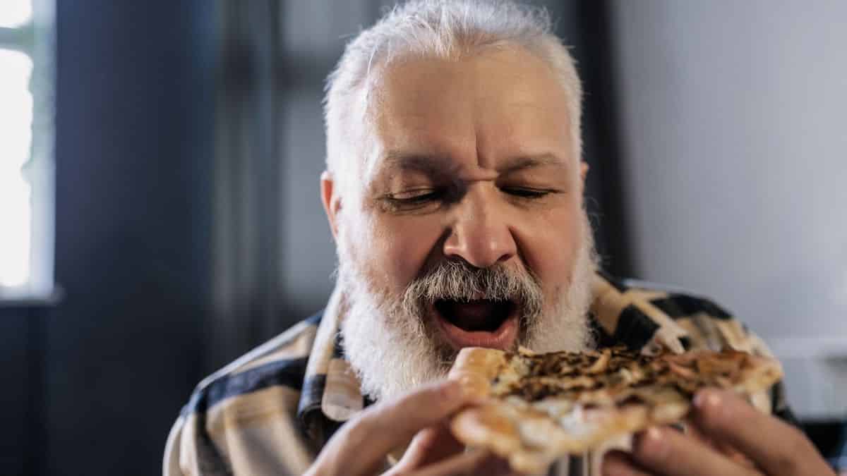 Photo of elderly male taking a bite of pizza