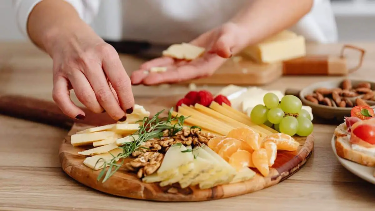 Hands placing food items onto a charcuterie board.