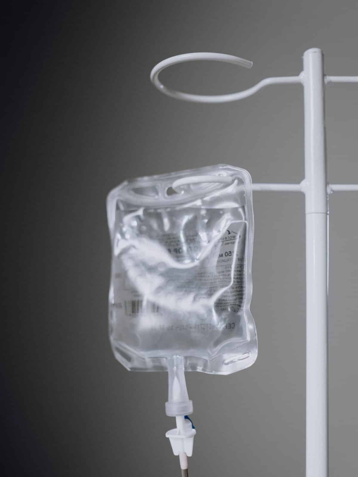 Photo of IV fluid bag hanging on white IV pole.