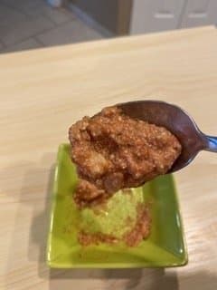 Meat sauce on a spoon being poured over a small green dish to show how thick it is.