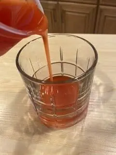 Moderately thick cranberry juice being poured into a clear glass. 
