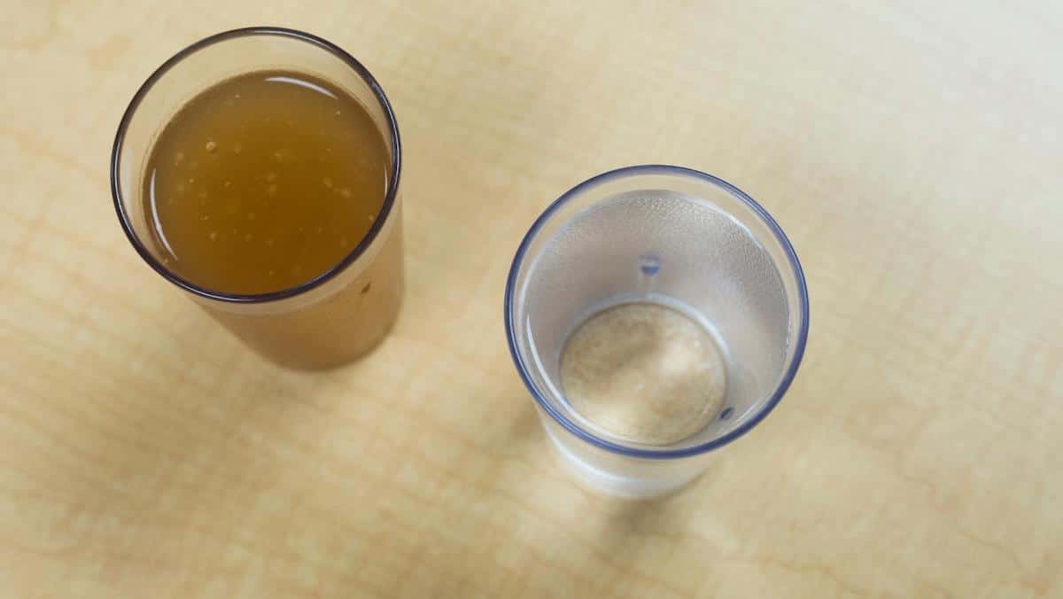 Thickened apple juice on the left and regular water on the right in clear cups on natural wood colored table.