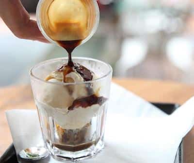Vanilla ice cream in clear glass with cold coffee being poured over top.