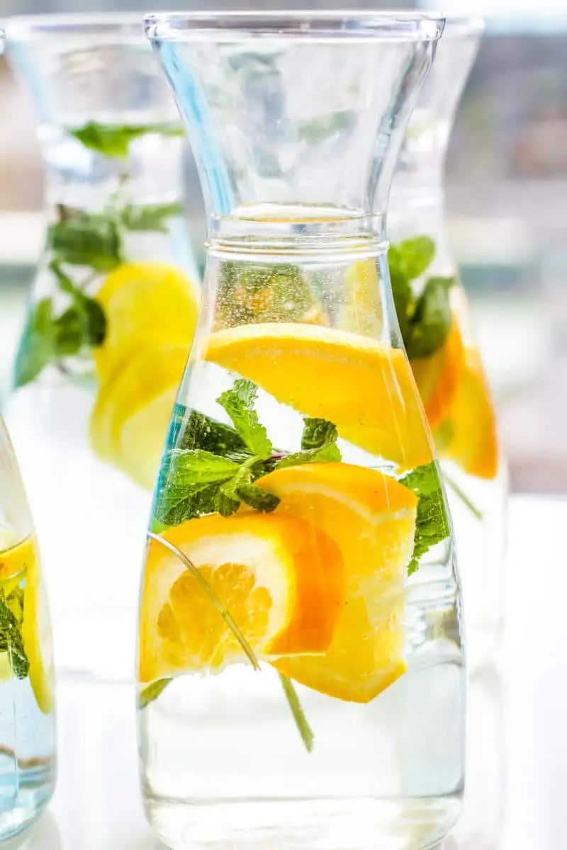 Water in clear carafes with slices of oranges and mint leaves in it.