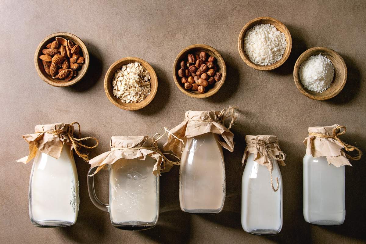 Milk alternatives in glass bottles with their coordinating source in small wooden bowls.