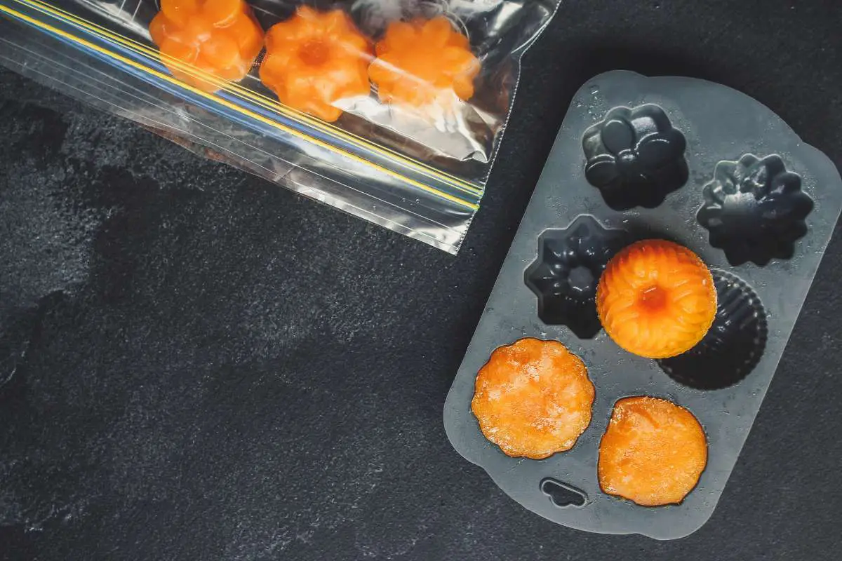 Grey pureed food mold with orange pureed food formed in it and some sitting next to it in a ziploc bag on a black counter. 