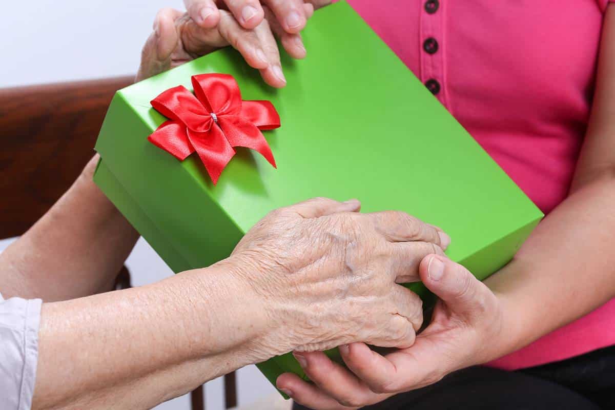 Younger hands handing older hands a gift wrapped in green paper with a red bow.
