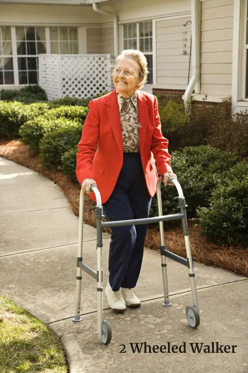 Older women wearing glasses in a red blazer walking outside with a two wheeled walker on a sidewalk smiling. 