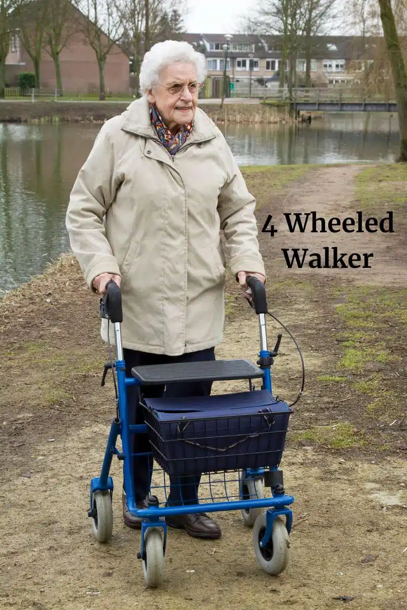 Older woman with white hair and glasses walking outside with a four wheeled walker wearing a beige coat near a river. 